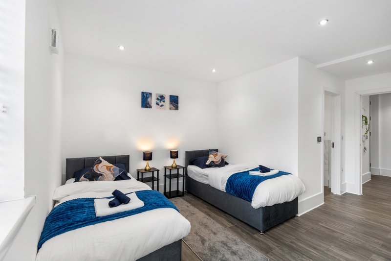 Bright modern bedroom with two single beds, blue bedding, wooden flooring and wall art