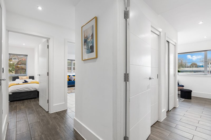 Bright hallway with white walls, dark wood flooring, and multiple white doors leading to bedrooms and other rooms