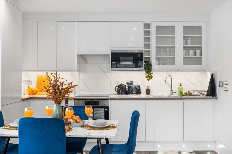 Modern white kitchen with dining table, blue chairs, marble backsplash and built-in appliances