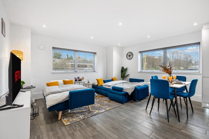 Modern open-plan living area with blue sofas, dining table, wooden flooring and large windows