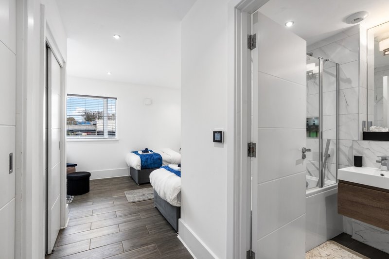 Modern bedroom with single bed, ensuite bathroom, white walls and dark wood flooring
