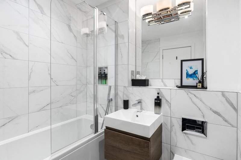 Modern bathroom with marble tiling, walk-in shower, vanity sink and framed blue artwork
