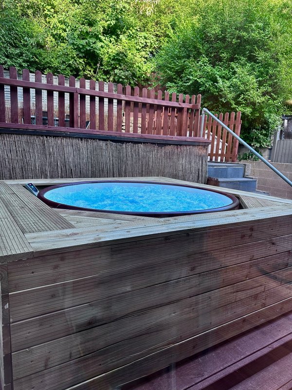 Outdoor deck with round blue hot tub, wooden railings and lush green trees