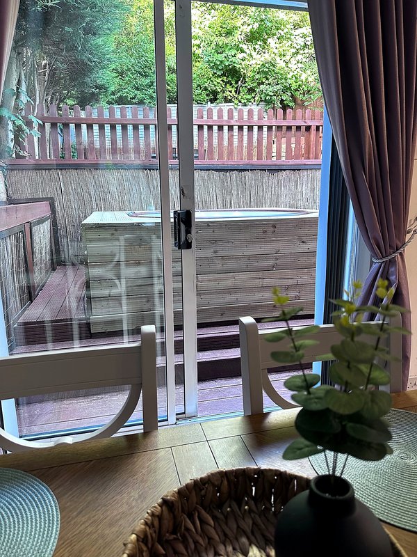 Interior view through glass doors to wooden deck with railing and garden beyond