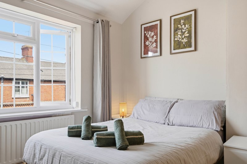 Bright bedroom with double bed, white bedding, framed botanical prints, and large window overlooking street