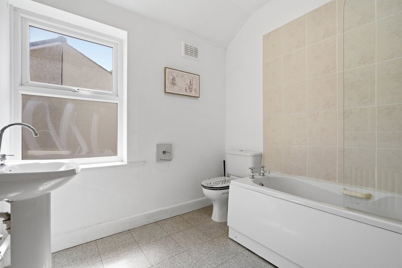 Bathroom with pedestal sink, bathtub, window, and beige tile walls