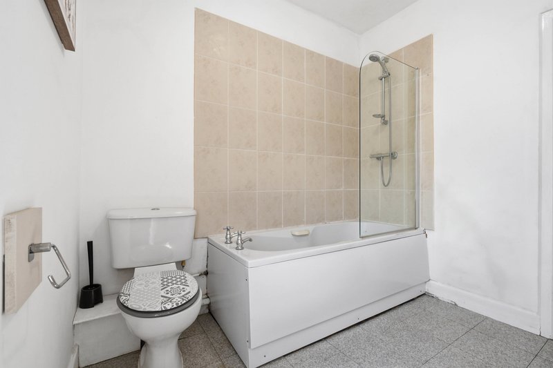 Modern bathroom with bathtub, glass shower screen, toilet, and beige tile walls