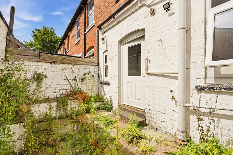 White-painted brick cottage exterior with door, window, and overgrown garden courtyard
