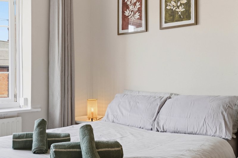 Bright bedroom with double bed, grey pillows, bedside lamp, window and botanical wall art
