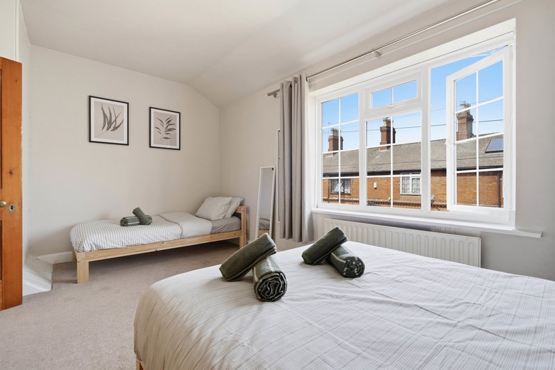 Bright bedroom with double bed, single bed, large window overlooking rooftops, and framed wall art