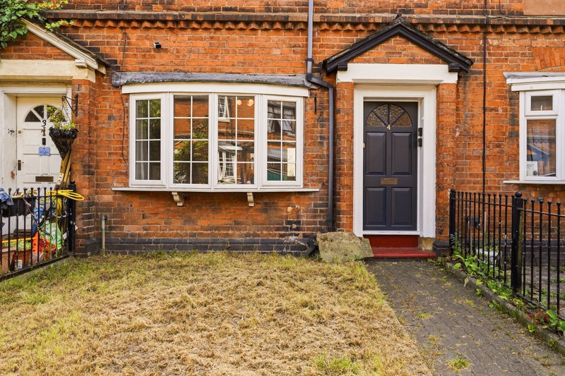 Red brick terraced house with bay window, dark front door, small front garden and driveway