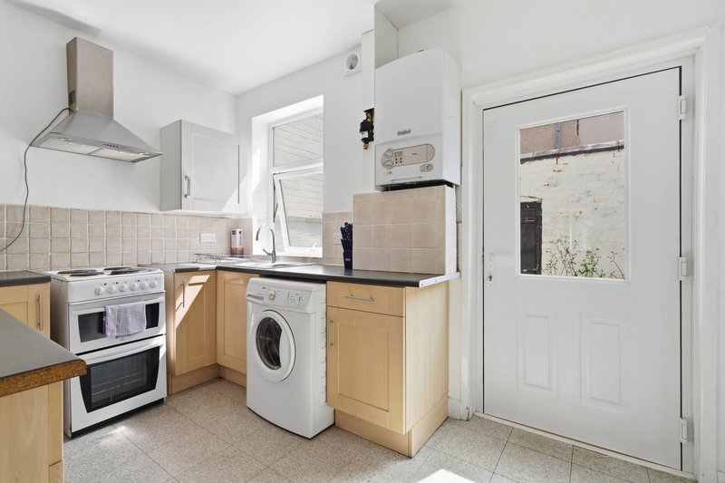 Compact kitchen with wooden cabinets, white appliances, beige tiles and door to garden