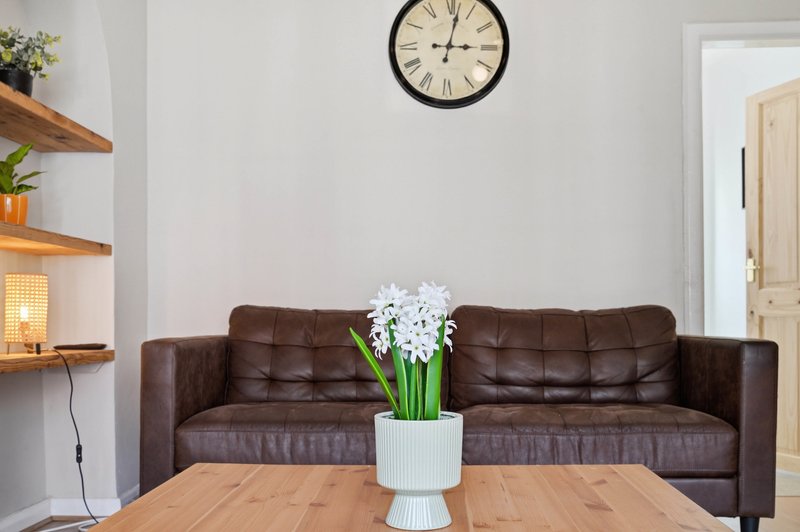 Living room with brown leather sofa, wooden coffee table, white flowers, wall clock and shelving