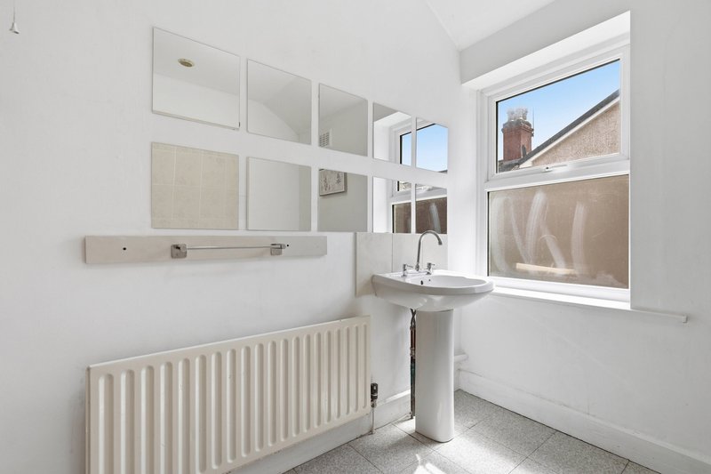 Bright bathroom with white radiator, pedestal sink, mirror cabinet and window with urban view
