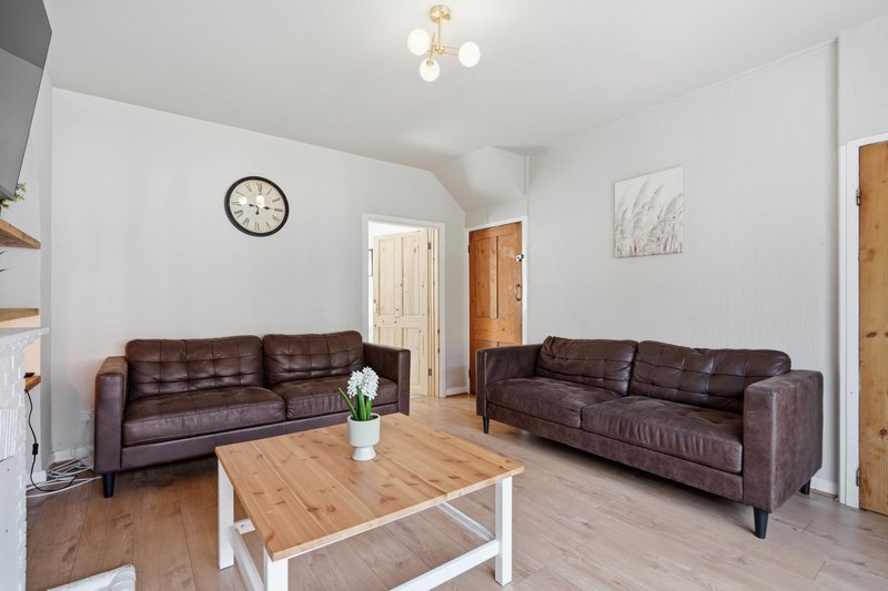 Spacious living room with two brown leather sofas, wooden coffee table, and wall clock