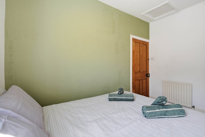 Minimalist bedroom with white bed, sage green wall, wooden door and radiator