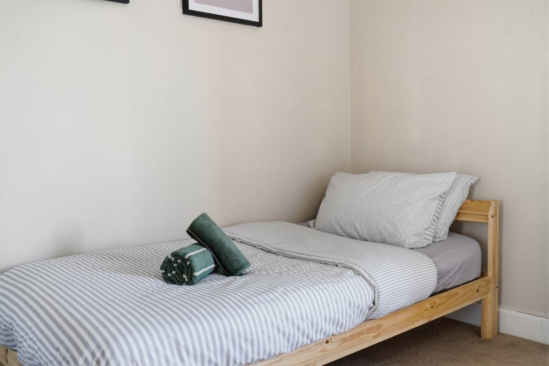 Single bed with striped bedding, wooden frame, and decorative pillows in bright room