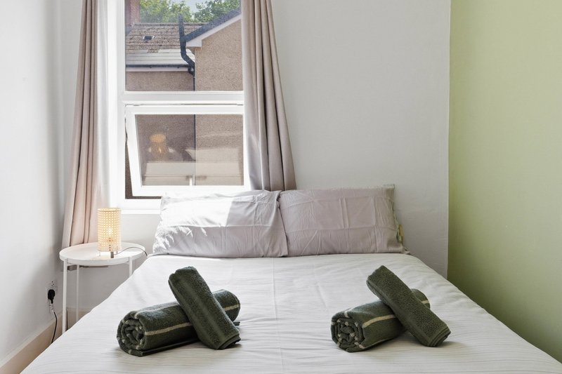 Bright bedroom with double bed, green accent wall, window with curtains and bedside lamp