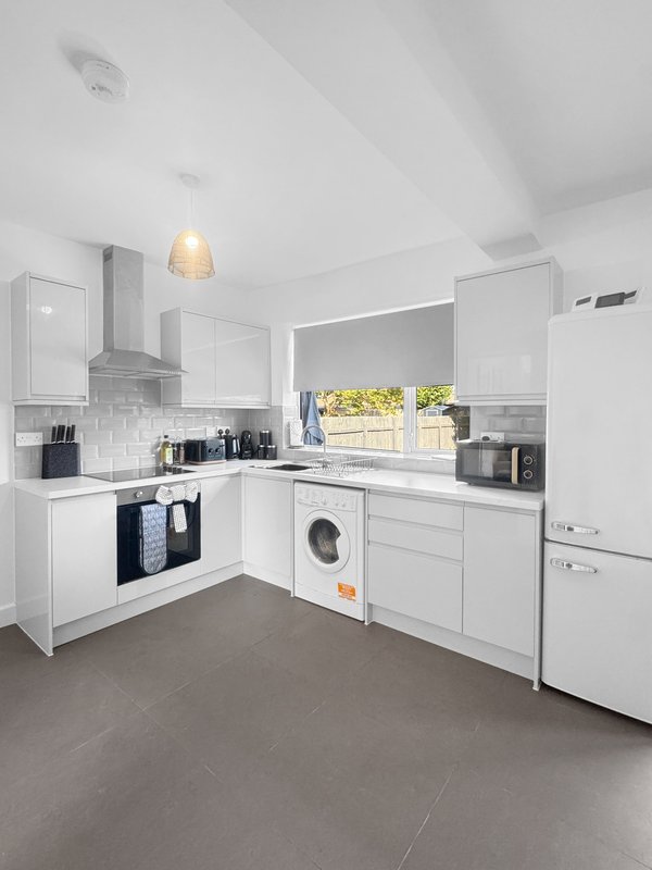 Modern white kitchen with appliances, dark worktops, pendant light and grey floor