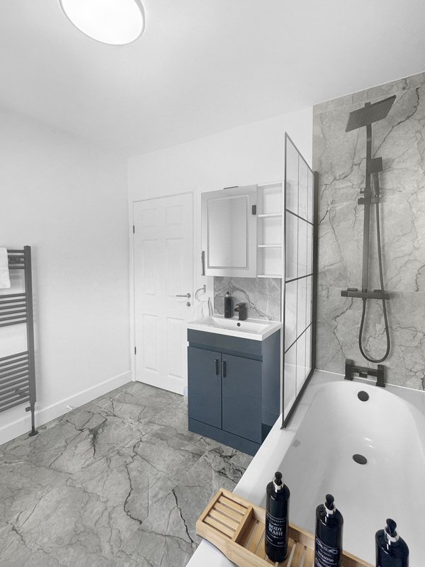 Modern bathroom with marble flooring, dark vanity unit, walk-in shower and freestanding bathtub