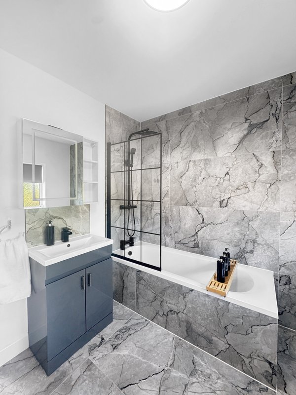 Modern bathroom with grey marble walls, vanity sink, bathtub and glass shower screen