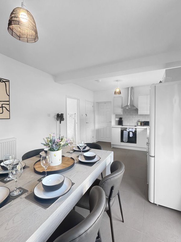 Modern open-plan kitchen and dining area with white cabinetry, dining table set for two, and pendant lighting