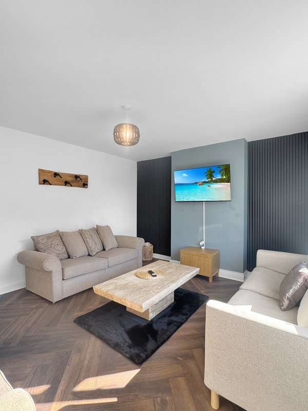 Modern living room with beige sofas, wooden coffee table, wall-mounted TV, and herringbone flooring