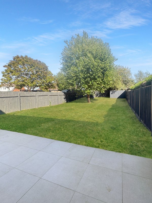 Large garden with paved patio, manicured lawn, mature trees and wooden fence boundaries