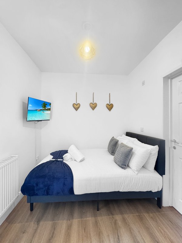 Bright bedroom with double bed, blue velvet throw, white pillows, wall-mounted TV, and decorative hearts