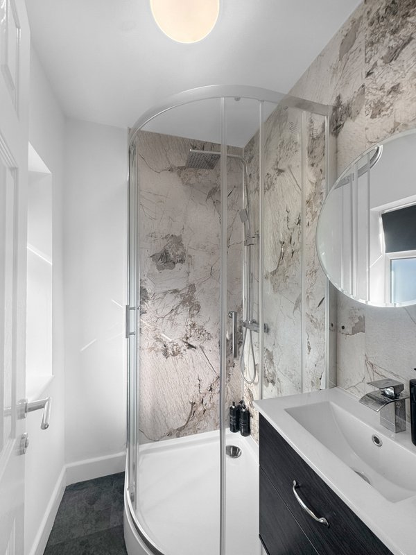 Modern bathroom with curved shower enclosure, marble-effect tiles, white sink and round ceiling light