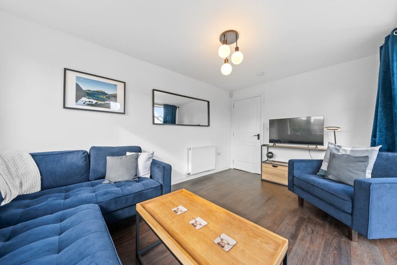 Bright living room with blue sofas, wooden coffee table, TV, and framed artwork on walls