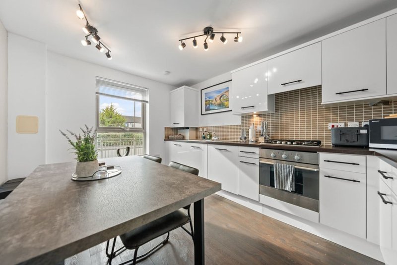 Modern kitchen with white cabinetry, grey countertop, dining table and window with garden view