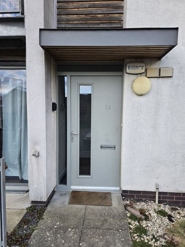 Modern grey entrance door with covered porch, small window, and light fixture