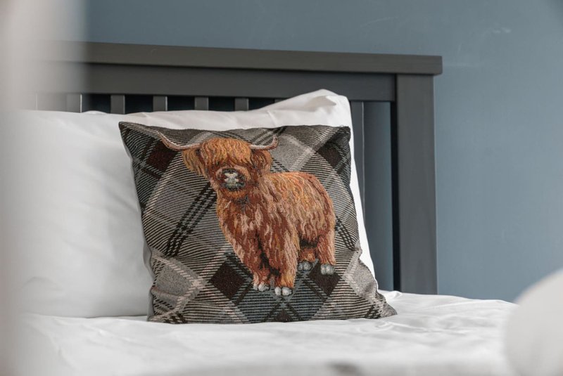 Bedroom with white pillows and decorative cushion featuring Highland cattle design