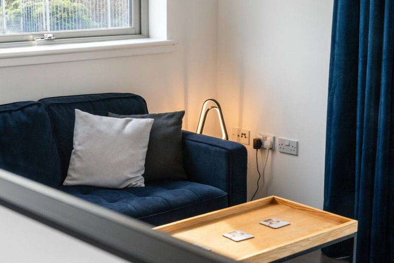 Modern living room with dark blue sofa, cushions, wooden coffee table and window