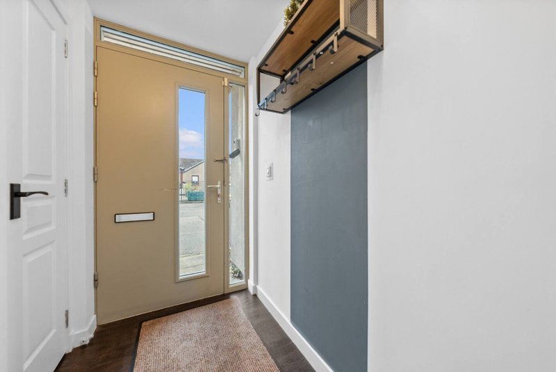 Hallway entrance with tan door, white walls, wooden floor and coat hooks