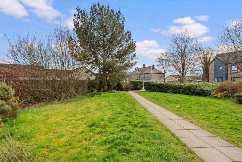 Garden pathway with green lawn, mature trees, and stone cottages in background