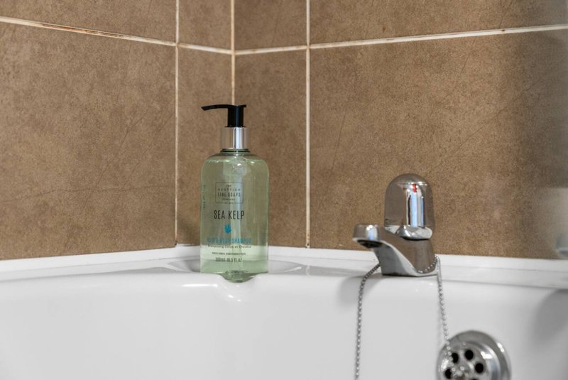 Bathroom sink with soap dispenser, faucet, and shower head against tiled wall