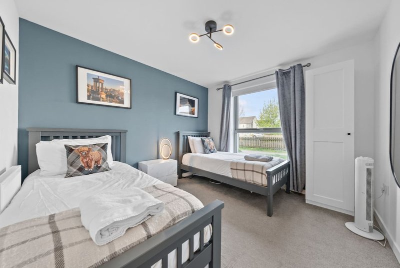 Bright bedroom with two single beds, blue accent wall, framed artwork and windows with garden view