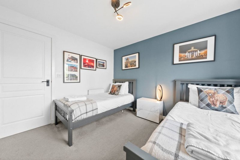 Bedroom with two single beds, blue accent wall, framed pictures, and white door