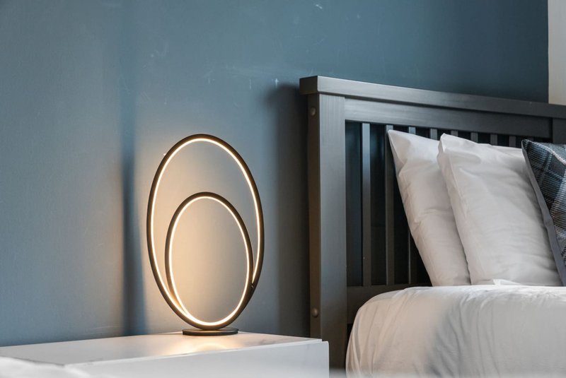 Modern bedroom with black bed frame, white pillows, and contemporary oval pendant light