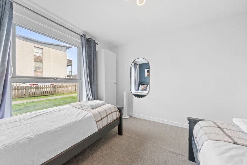 Bedroom with two single beds, large window overlooking garden, and wall-mounted mirror