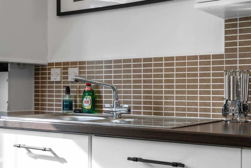 Modern kitchen with brown tile backsplash, stainless steel sink, faucet and utensil rack