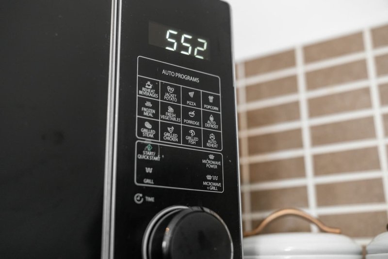 Close-up of microwave control panel with digital display and buttons, window visible in background