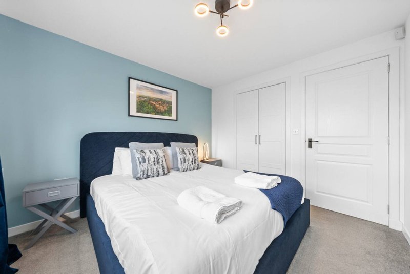 Bedroom with blue upholstered bed, white bedding, blue accent wall and white wardrobe doors