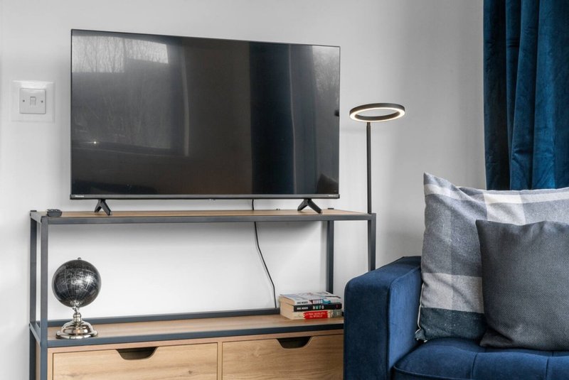 Modern bedroom with wall-mounted TV, metal shelving unit, wooden drawers, globe, and blue upholstered sofa