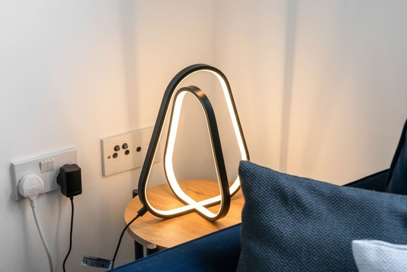 Bedroom corner with neon desk lamp, electrical outlets, and blue textured bedding