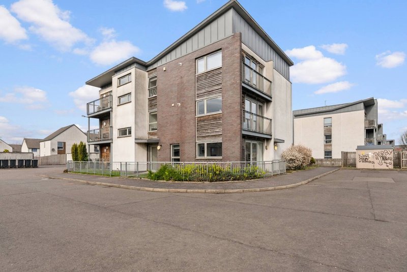 Modern multi-story residential apartment building with brick and metal cladding, parking area and landscaping