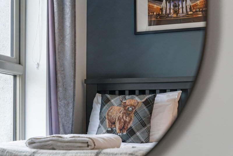 Bedroom alcove with dark headboard, plaid cushion with dog design, and window with curtains
