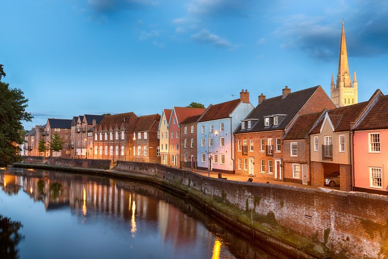 Riverside town with colorful historic buildings, church spire, and calm water reflection at dusk